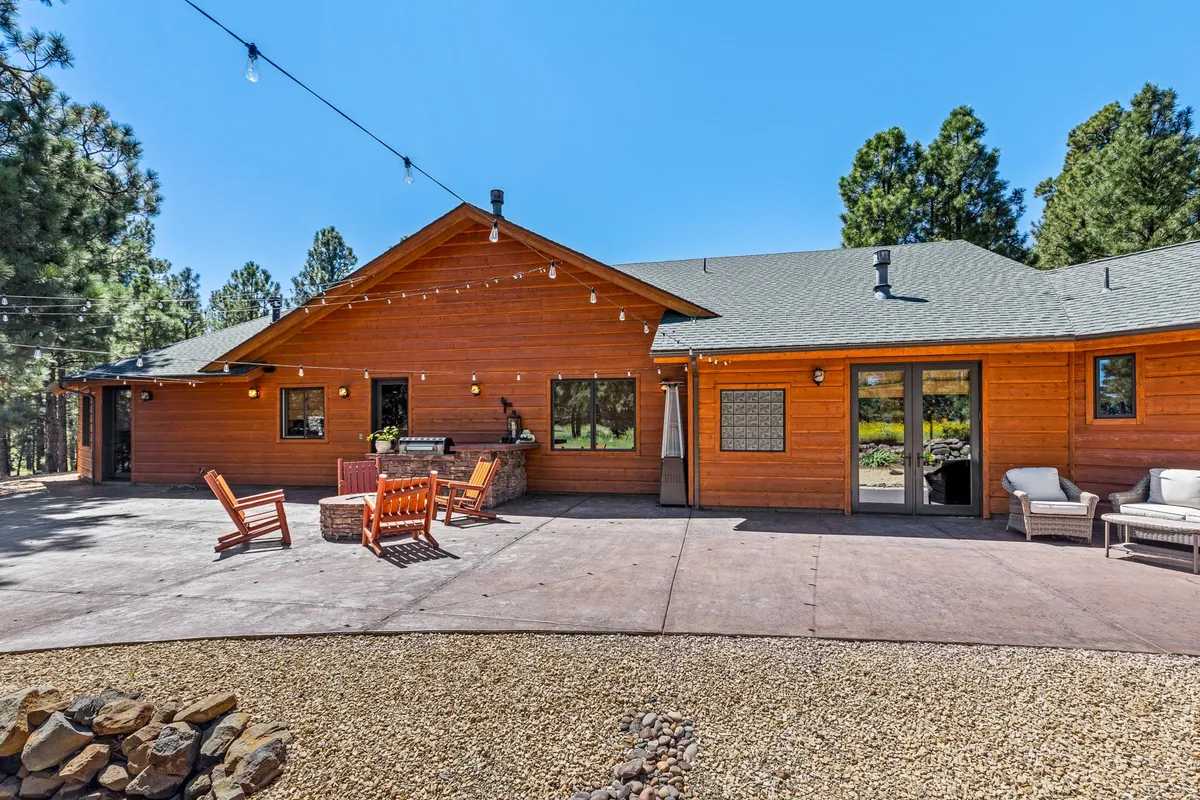 A private patio area outfitted with wooden furniture, string lights, and lush natural landscaping, ideal for outdoor relaxation and gathering. Large windows connect the patio to the interior, creating seamless indoor-outdoor living.