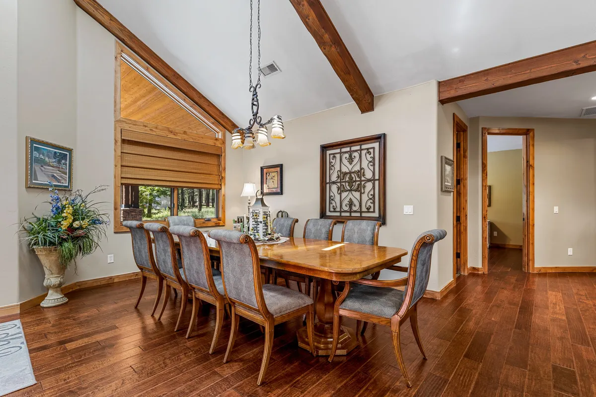 This interior image highlights a large dining table beneath wooden beams, decorated with a floral arrangement and art, bathed in natural light. The scene captures a warm, communal atmosphere ideal for group meals and celebrations.