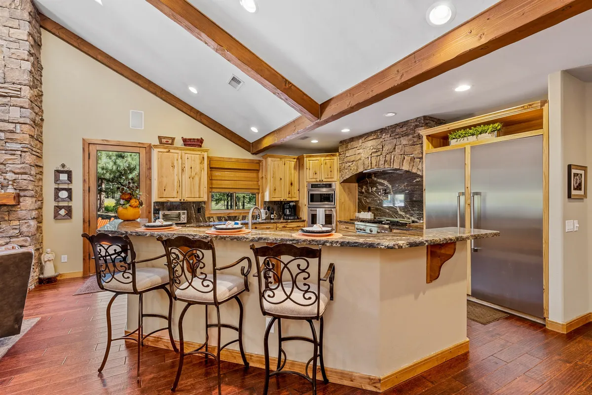 A spacious and stylish kitchen with a central island, granite countertops, wooden cabinetry, bar stools for casual seating, and a stone accent wall. The layout encourages both cooking and socializing, ideal for holiday meals or Sunday brunches.