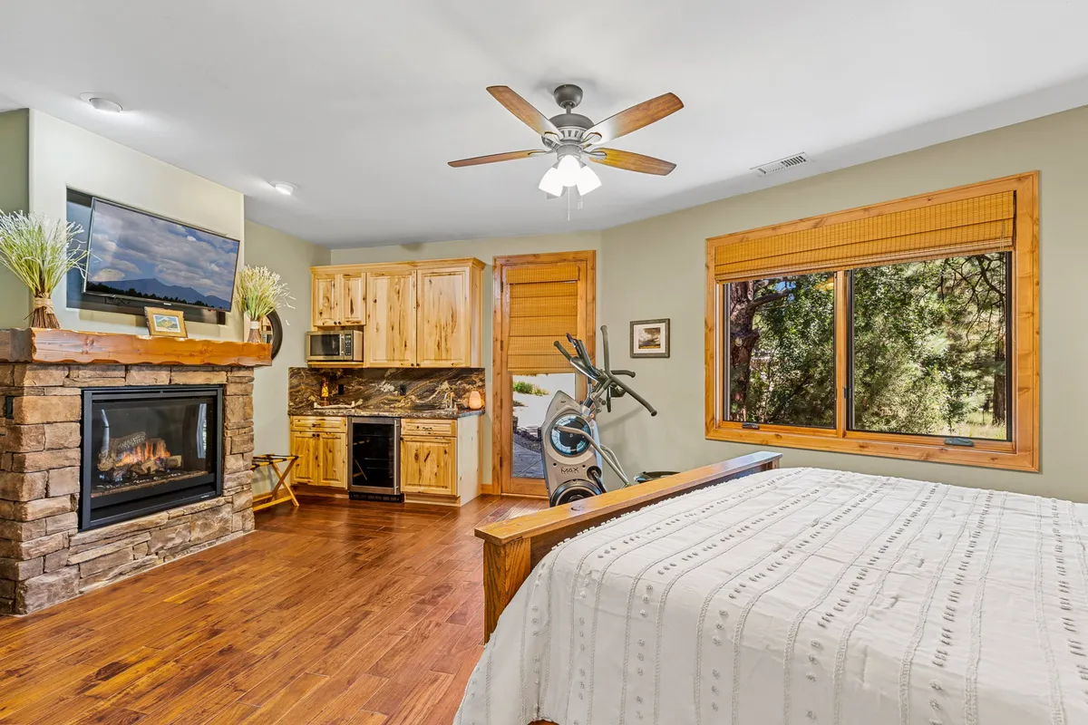 A spacious guest suite showcasing a plush bed, a cozy fireplace, large windows with outdoor views, and elegant wooden cabinetry. The inviting ambiance is perfect for relaxation, with the fireplace adding both warmth and a sense of luxury.